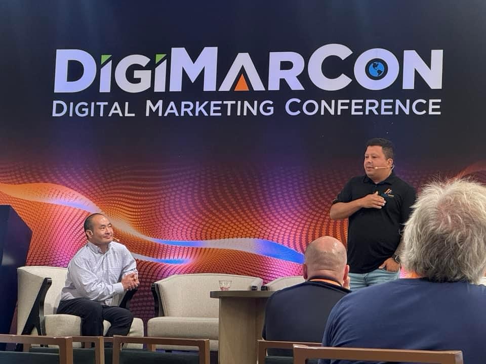 Nilson Silva explains critical offline marketing strategies while Dennis Yu listens in at DigiMarCon Miami.