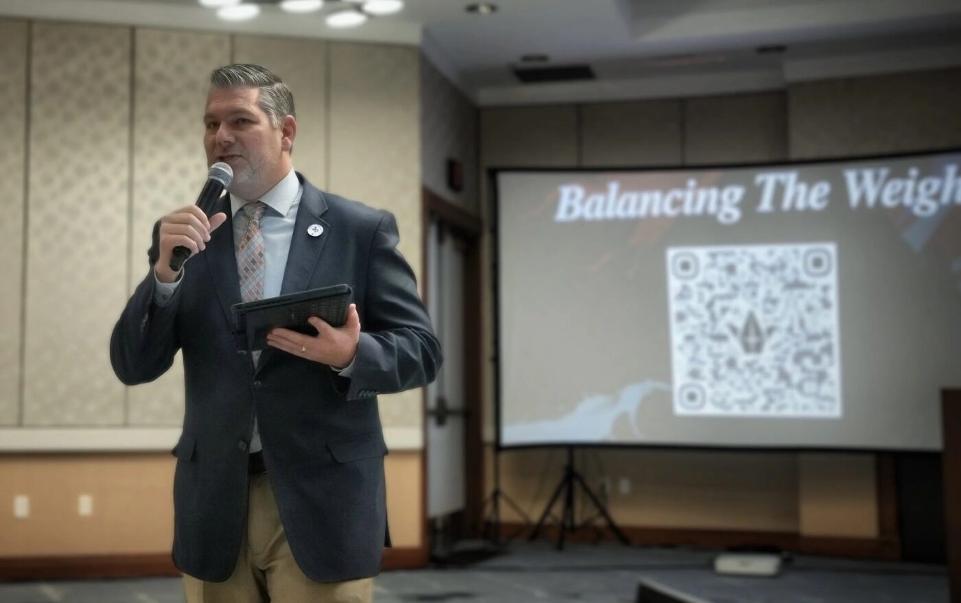Pete Hazzard presenting beside a screen with a microphone and tablet
