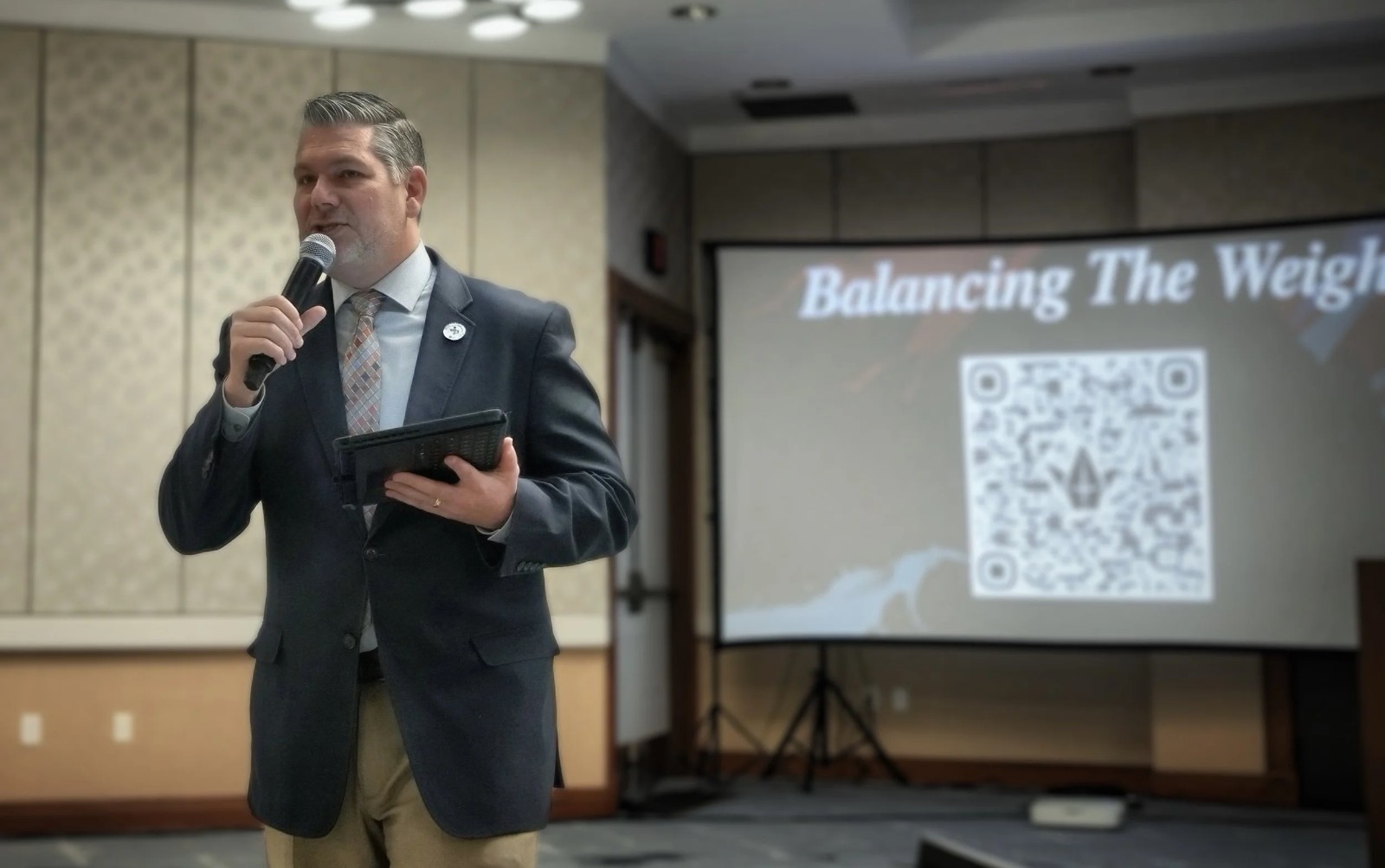 Pete Hazzard presenting beside a screen with a microphone and tablet